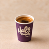 A purple paper coffee cup with 'Halo Bagels Cafe' printed in white, filled with espresso and set on a beige surface against a matching beige background.
