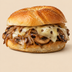 A close-up of a gourmet cheeseburger with sautéed mushrooms, caramelized onions, melted cheese, and a golden-brown bun on a solid beige background.