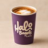 A purple paper coffee cup with the 'Halo Bagels CAFE' logo printed in white, filled with a cappuccino topped with milk foam, set against a neutral beige background.