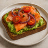 Avocado toast with salmon, tomatoes, and onions on a white plate. halo bagels harlem