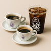 Two cups of coffee and a glass of iced coffee with Halo Bagels logo on a beige background best coffe in nyc harlem